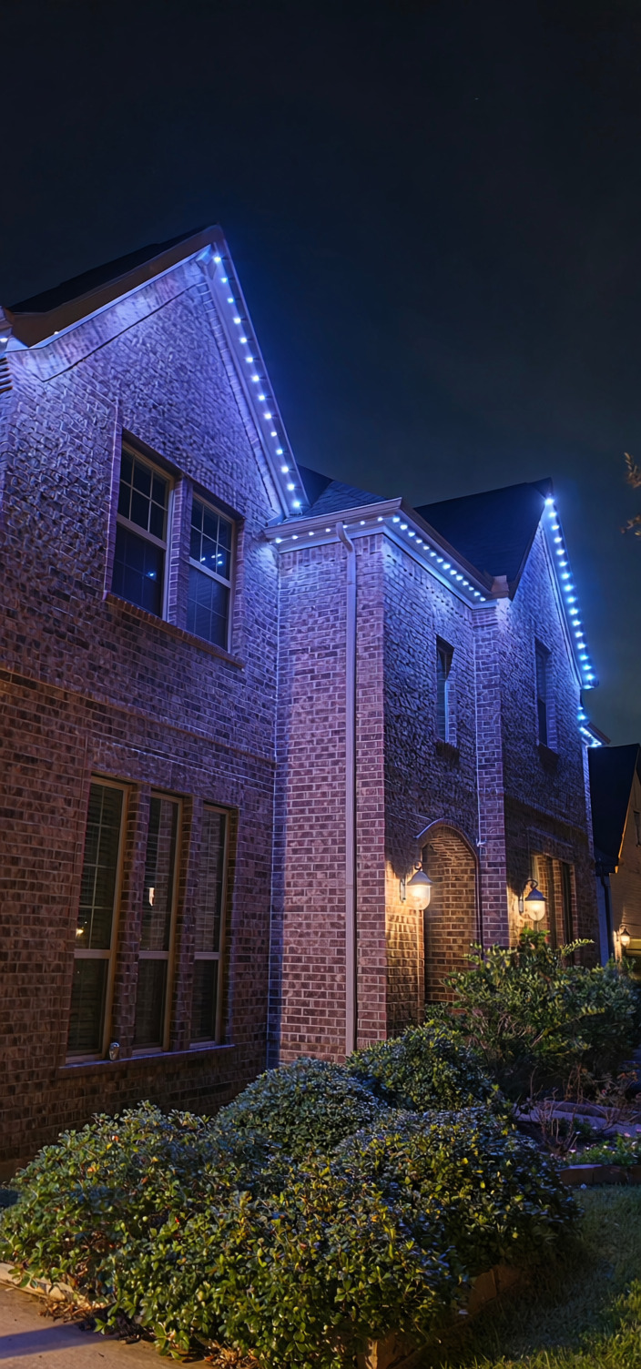 Blue and white permanent lights installed along the gables and eaves of a brick home
