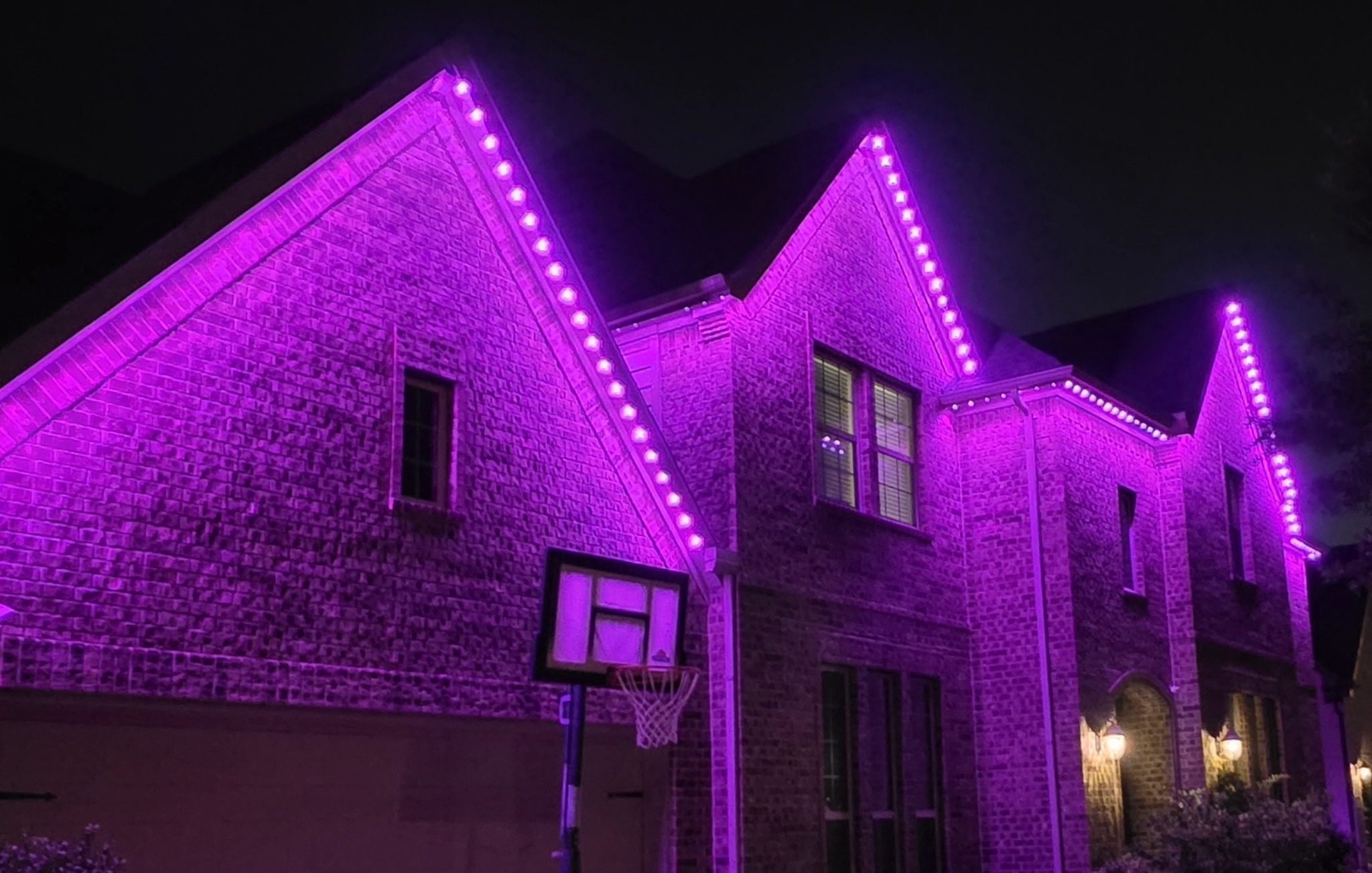 Purple permanent lighting covering the complete roofline of a two-story brick home